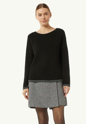 Schwarzer Rippsweater mit weiter Halslinie, kombiniert mit einem grauen Fischgrätrock mit gefaltetem Design und einem glitzernden Saumdetail.