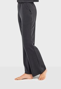 Schwarze, locker sitzende Hose aus weichem Stoff; mit elastischem Bund und Seitentaschen; ausgestelltes Bein-Design; barfuß getragen.