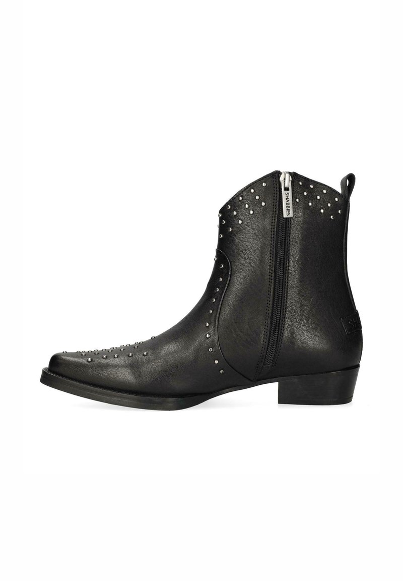 Botas de tobillo negras de cuero, con tachuelas plateadas, punta afilada y cremallera lateral para el cierre. Textura suave con tacón bajo.