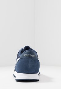 Laivansininen Reebok-kengät, joissa on mokka- ja verkkomateriaalit, pyöristetty muoto, valkoinen välipohja ja voimakas logo kannassa.