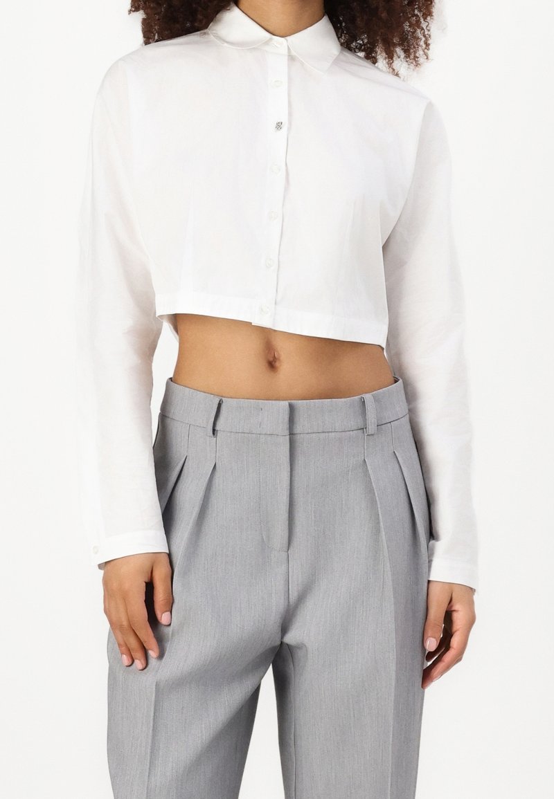 Witte cropped button-up shirt met lange mouwen, voorzien van een kleine kraag en een enkele knoopaccent. Grijze hoge taille geplooide broek.