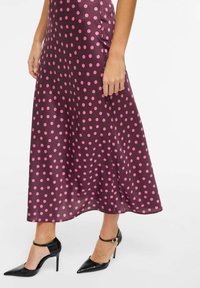 Vestido midi de satén en púrpura oscuro con lunares rosas. Presenta un dobladillo acampanado y se lleva con tacones negros de punta afilada y correas en el tobillo.