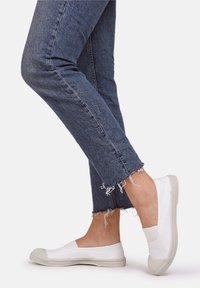 Chaussures blanches à enfiler avec une semelle texturée, associées à un jean denim bleu effiloché, avec une coupe fuselée et un ourlet brut.