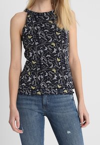 Top senza maniche blu navy con stampa floreale e di farfalle, caratterizzato da un tessuto testurizzato e un leggero volant all'orlo. Abbinato a jeans blu.