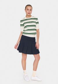 Wit en groen gestreept sweater met korte mouwen en een aansluitende taille, gecombineerd met een marineblauwe geplooide rok en witte sneakers.