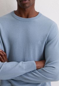 Jasnoniebieski dziergany sweter z okrągłym dekoltem, ściągaczami na rękawach oraz subtelnym logo na piersi, charakteryzujący się miękką teksturą i dopasowanym krojem.