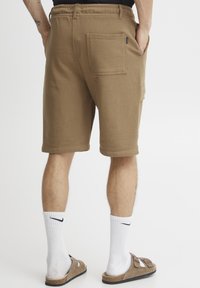 Braune Baumwollshorts mit einem elastischen Bund, seitlichen Taschen und einer hinteren aufgesetzten Tasche. Einfache Struktur mit einem knielangen Schnitt.