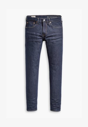 Jeans en denim bleu foncé avec une coupe slim. Les caractéristiques incluent une fermeture éclair, cinq poches et des coutures contrastées le long des coutures.