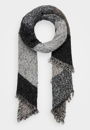 Écharpe tricotée noire, grise et blanche avec des blocs de couleur diagonaux et des extrémités à franges, enroulée en forme circulaire sur fond blanc.