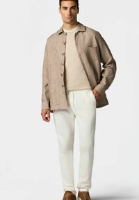 Hnědá lněná košile s knofl íky, béžový svetr pod ní, bílé kalhoty a hnědé boty. Jednoduchý design s kapsou na hrudi.