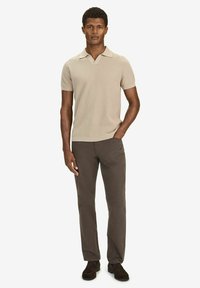 Beige kortärmad polo med ribbat mönster och en platt krage, i kombination med mörkbruna byxor och bruna mockaskor.