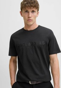 Crna pamukasta majica s kratkim rukavima, okruglim izrezom i teksturiranim logotipom "JACK&JONES PREMIUM" na prednjoj strani.