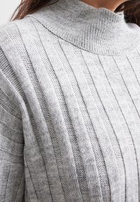 Grauer hochgeschlossener Pullover mit gerippter Textur, abwechselnd vertikalen Streifen und aus weichem Strickmaterial.