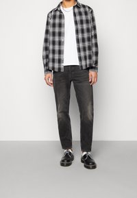 Sorte og hvide ternet skjorte over en hvid T-shirt, parret med mørke jeans og sorte sko med hvide accenter. Afslappet pasform, knappet skjortedesign.