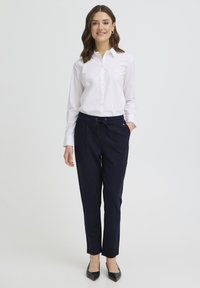 Cămașă albă cu nasturi, pantaloni bleumarin cu talie reglabilă prin șnur, pantofi negri. Material neted, croială ajustată, design cu picior drept.