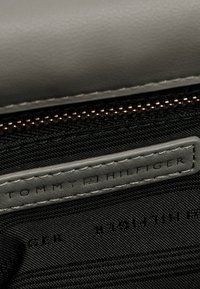 Interno di portafoglio in pelle grigia con fodera in tessuto nero, con chiusura ZIP visibile, etichetta "TOMMY HILFIGER" in rilievo e cuciture fini.