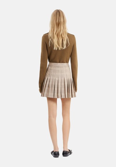 Bruine wollen trui gecombineerd met een geplooide beige geruite rok. Bevat een aansluitende taille en zwarte loafers. Zichtbare achterkant.