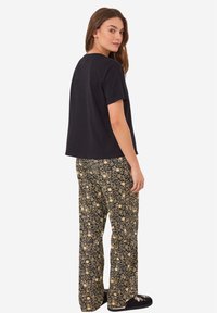 Zwarte t-shirt met korte mouwen, gecombineerd met losse bloemenmotieven broek in een zwart en gouden kleurenschema.