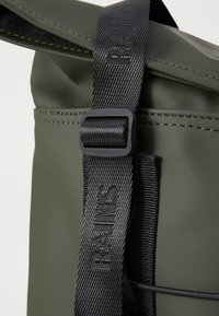 Olivegrünes, wasserdichtes Rucksackmaterial mit einem schwarz verstellbaren Tragegurt, der geprägt ist. Glatte Textur und nahtlose Kanten.