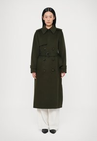 Dubbelgeknoopte, lange olijfgroene jas met een ceintuur in de taille, grote kraag en voorzakken, gemaakt van een gestructureerde stof.