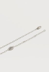 Ασημένιο κολιέ με αλυσίδα από οβάλ κρίκους, κυκλικό μεταλλικό ταμπελάκι με χαραγμένα γράμματα και κούμπωμα με κλαγκτ αστακό σε λευκό φόντο.