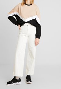Sweatshirt en color-block beige, noir et blanc ; associé à un jean blanc taille haute ; baskets noires à semelle épaisse.