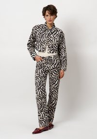 Geknipte jas en bijpassende broek in een cr�èmekleurig en zwart abstract golfpatroon, met knoopdetails en een strakke pasvorm. Echte leren schoenen.