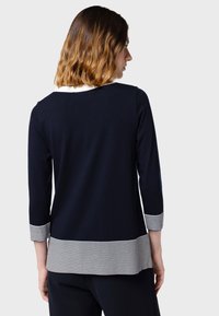 Maglione blu navy con maniche a tre quarti, caratterizzato da un orlo inferiore a righe bianche e blu navy. Texture liscia e design casual.