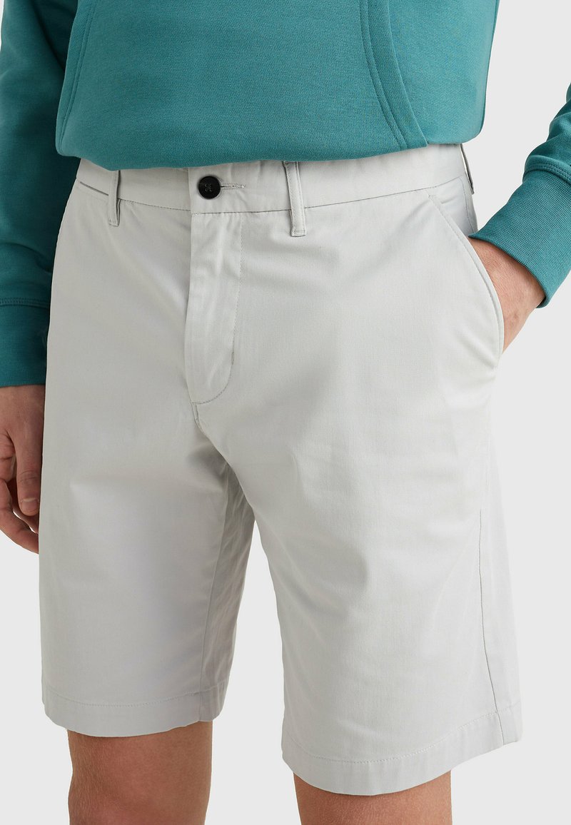 Pantaloni corti grigi chiari realizzati in tessuto liscio, con un frontale piatto, tasche laterali e chiusura con un solo bottone. Design casual e versatile.