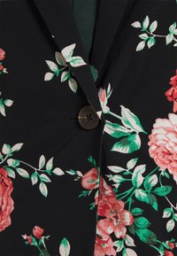 Blazer negro con estampado de hojas verdes y flores rosas, que presenta un solo botón oscuro y una tela texturizada.