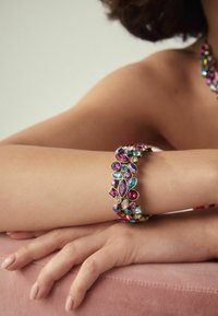 Multicolored gemstone bracelet featuring pink, blue, and gold accents, with various shaped stones set in a gold-tone metal band.