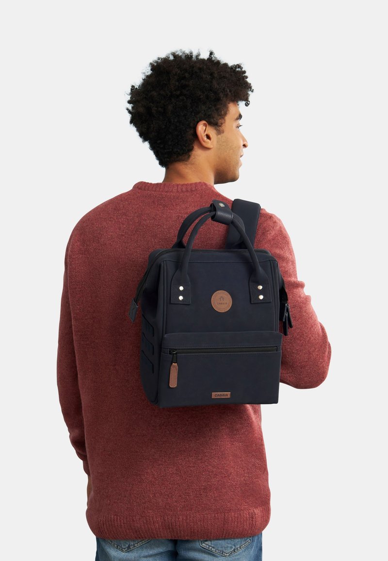 Marineblauwe rugzak met een gestructureerde afwerking, bovenhandvatten, gevoerde schouderband, voorvak met rits en een ronde logo-accent.