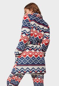 Fluffy white robe with red and blue geometric and heart patterns, belted at the waist, featuring long sleeves and two side pockets.
