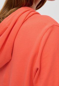 Koralröd hoodie med en mjuk textur, med en avslappnad passform och justerbar dragsko i huvan. Enkelt design utan synliga mönster.