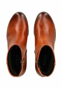 Bottines en cuir marron avec un design épuré, fermeture éclair latérale et bout rond. La doublure intérieure est foncée avec un logo visible. Semelle en caoutchouc noir.