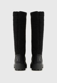 Botas negras hasta la rodilla con un upper de tejido texturizado y esponjoso y un inferior de cuero liso. Suelas de goma gruesas que proporcionan agarre y estabilidad.