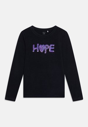 Chemise noire à manches longues avec col rond, ornée du mot « HOPE » écrit en sequins violets, avec un cœur remplaçant le « O ».