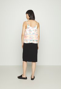 Camisola com estampado floral e alças finas, sobreposta a uma saia preta de comprimento até ao joelho. A parte de cima tem uma faixa estampada em rosa e azul na bainha.