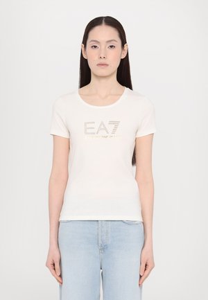 Witte katoen T-shirt met korte mouwen, ronde halslijn en metallic EA7-logo met strassteentjes aan de voorkant. Gecombineerd met lichtblauwe jeans.