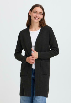 Lange zwarte cardigan van zachte stof, met een V-hals, twee voorkkoten en een open voorkant ontwerp. Draag het over een wit shirt.