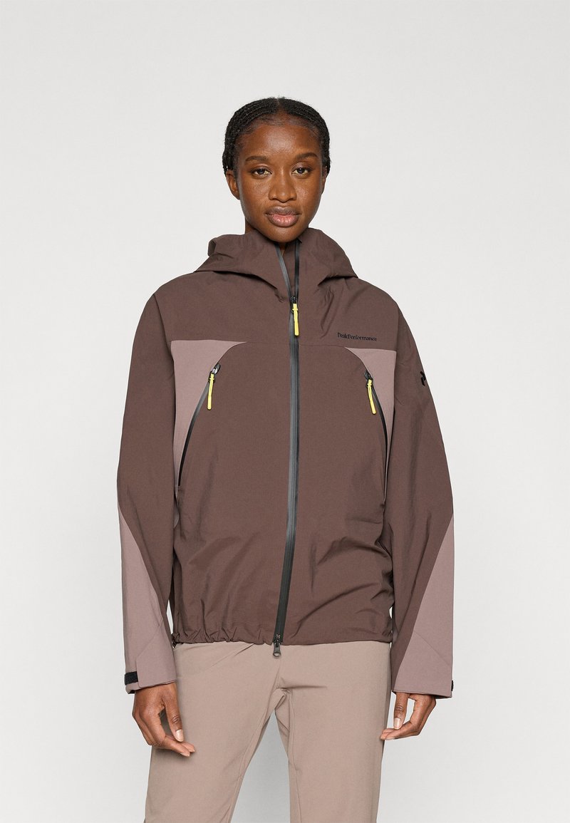 Καφέ αδιάβροχο μπουφάν με γκρι λεπτομέρειες, ρυθμιζόμενο καπό, τσέπες με φερμουάρ και ελαστικά μανίκια. Ελαφρύ, σχεδιασμένο για υπαίθρια δραστηριότητα.