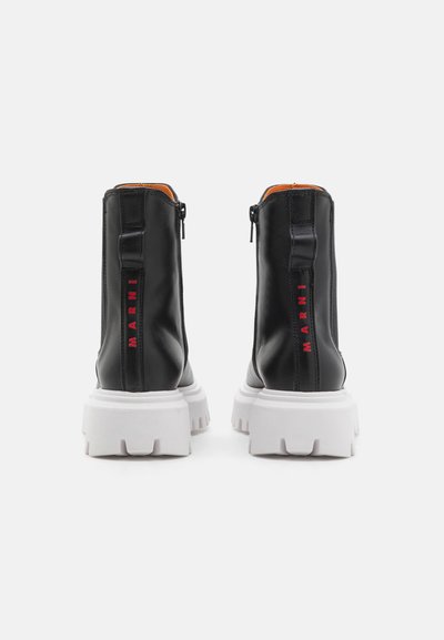 Botas de tobillo de cuero negro con una suela gruesa blanca, cremalleras laterales y el logotipo rojo "MARNI" en el talón. Acabado texturizado con forro naranja.