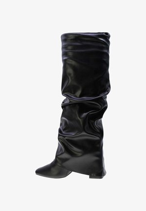 Stivale in pelle nero slouchy, alto fino al ginocchio, con punta affilata e tacco basso, isolato su sfondo bianco.