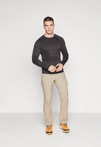 Juoda ilgomis rankovėmis sportinė palaidinė su raglano rankovėmis, derinama su šviesiai smėlio spalvos krovinių kelnėmis su šoninėmis kišenėmis ir oranžiniais sportiniais bateliais.