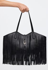 Bolso tote de cuero negro con detalles de flecos largos, correas dobles y cierre central de herrajes plateados. Textura suave, base ancha.