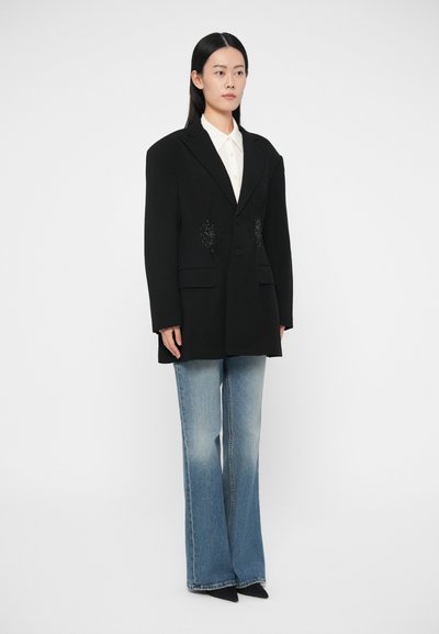 Černé sako s gepardím střihem, klopy s výstřihem do zářezu, dvě kapsy a ozdobné detaily. Kombinováno s lehce modrými zvonovými džínami.