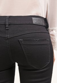 Jeans de mezclilla negra con una textura suave, que presentan un diseño de bolsillo trasero bien definido y costuras en contraste. Etiqueta de cuero negro en la cinturilla.