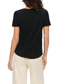 Czarna koszulka z krótkim rękawem, wykonana z miękkiej bawełny, z okrągłym dekoltem i luźnym krojem, przedstawiona od tyłu z jasnymi spodniami.