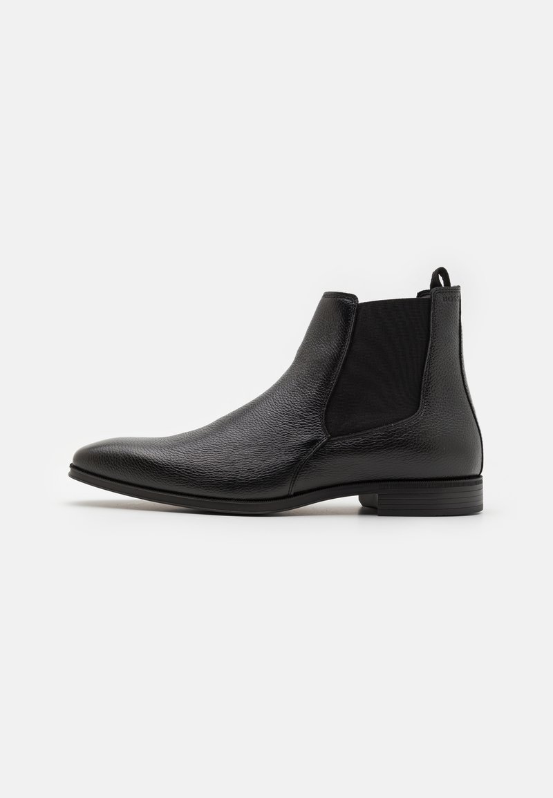 Bottes Chelsea en cuir noir avec une finition texturée, panneaux élastiques sur les côtés, bout arrondi et petit talon carré. Design minimaliste avec une languette de tirage.