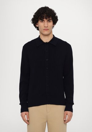 Cardigan din tricot cu nervuri de culoare bleumarin, cu guler, nasturi pe toată lungimea din față și mâneci lungi. Are o textură netedă și o siluetă ajustată.